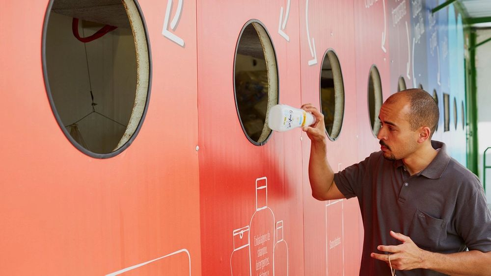 Un homme dépose une bouteille en plastique dans un grand mur de recyclage coloré.